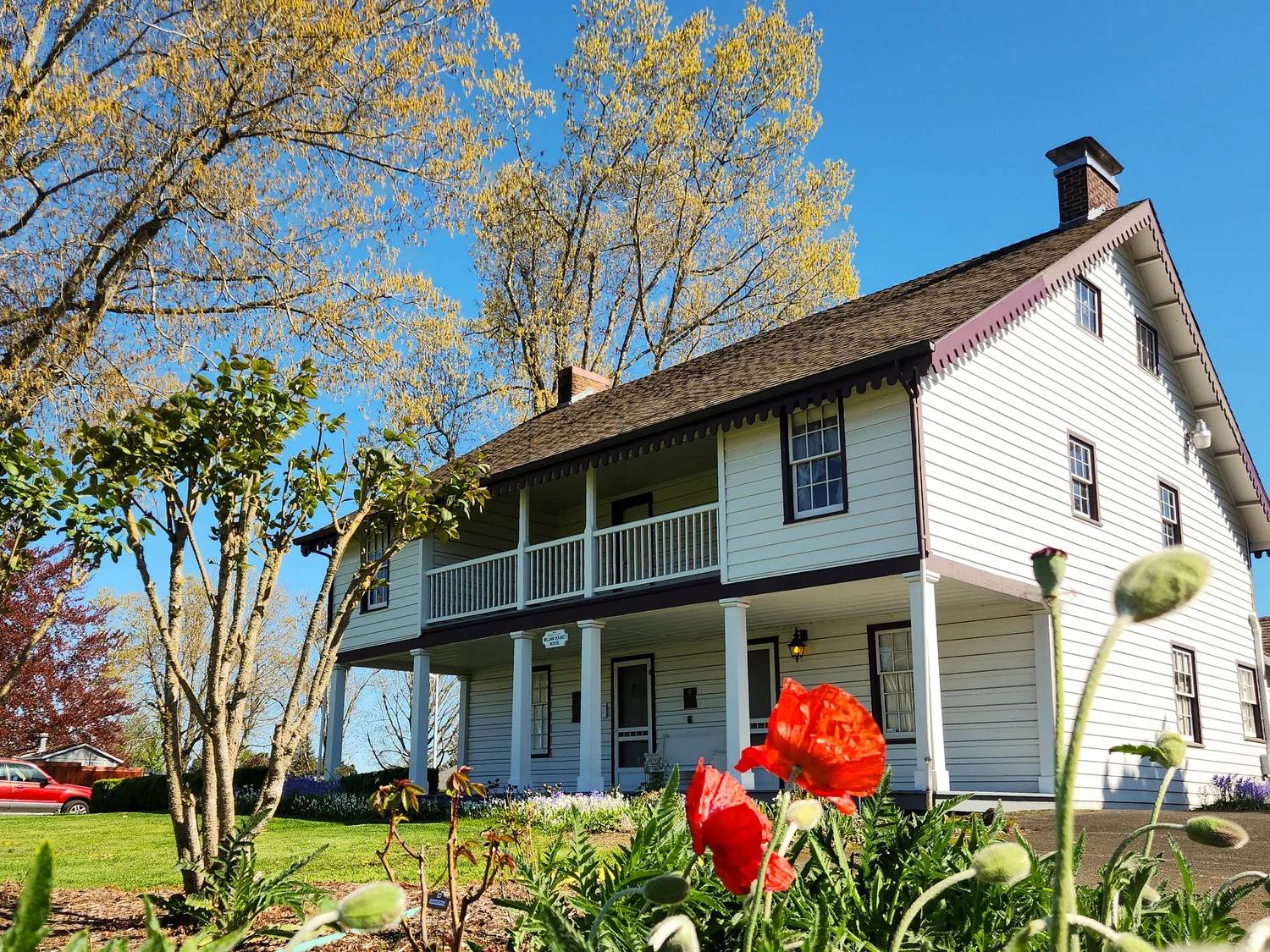 The William L. Holmes House at the Rose Farm on a clear spring morning, with red poppies in the garden bed below its two storey porch.